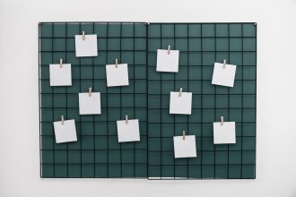 A black metal grid board, ideal for enhancing corporate culture, is mounted on a white wall and displays ten blank white square notes attached with small wooden clothespins. The board has a green background and is divided into two sections.